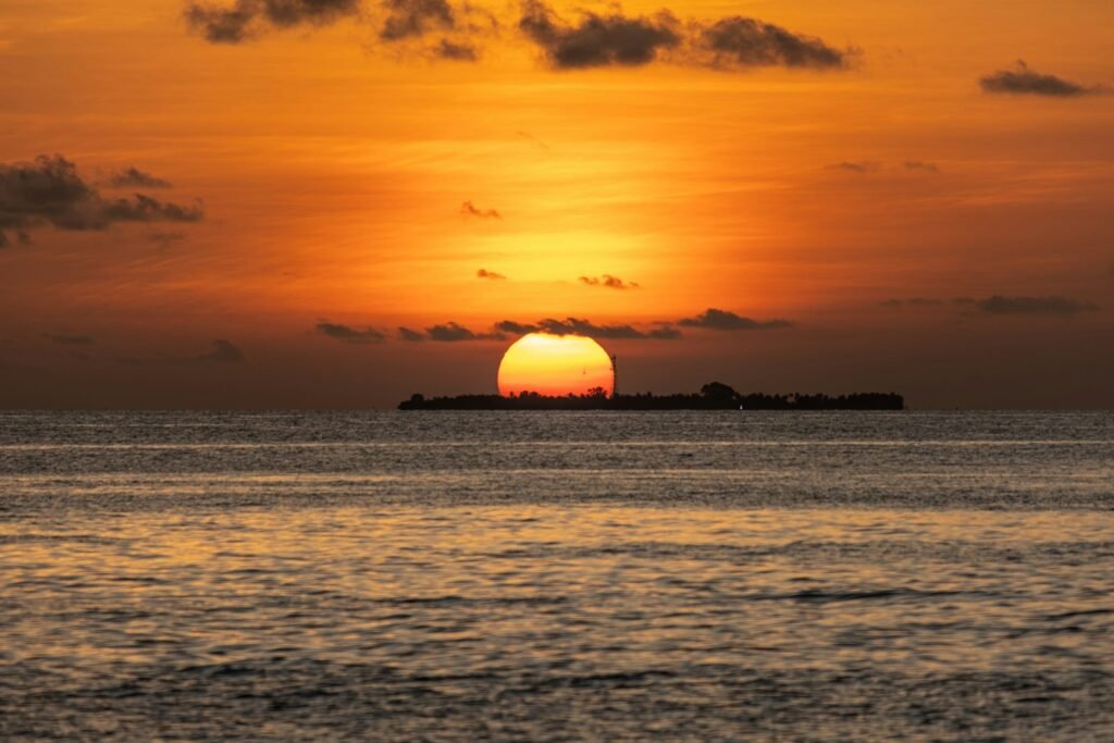 Sun setting over ocean with distant island silhouette, Maldives
